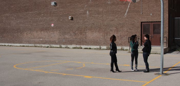 Three young people are standing in a basketball court and talking to each other.