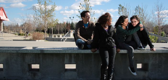 Four young people sitting together in a park talking to each other.